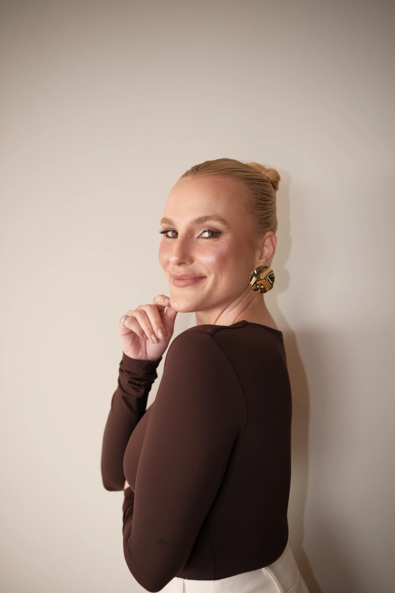 Gabriela Wiggers, de body marrom, olhando para a câmera por cima do ombro e sorrindo